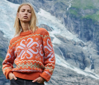 Woman standing in front og glacier wearing Falkeberg sweater in vibrant orange with decorative pattern