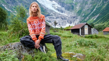 Woman sitting on rock in lush Norwegian nature with glacier an small farm houses in backround.